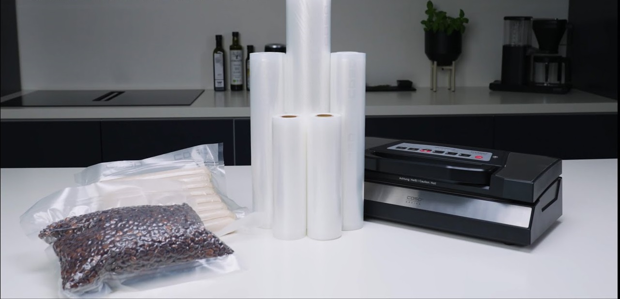 Vakuumiergerät mit Rollen und verpackten Lebensmitteln auf weißem Tisch