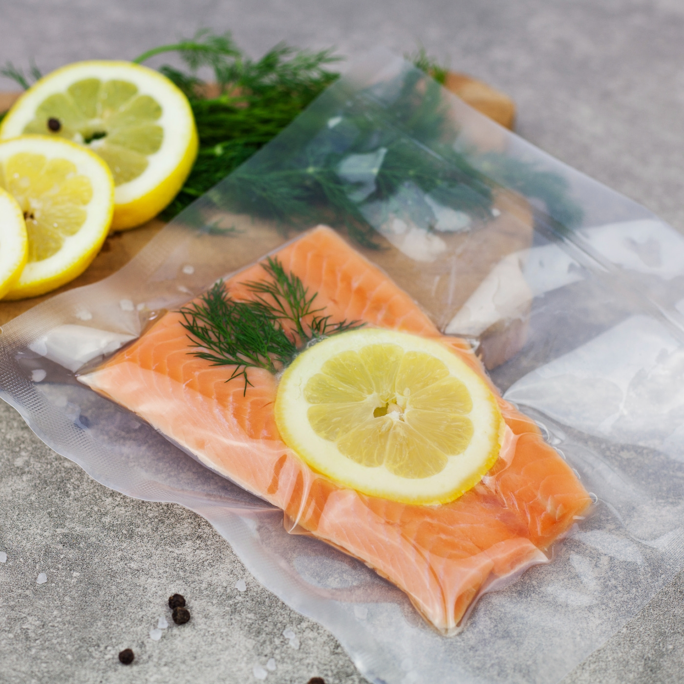 Lachsfilet mit Zitrone und Dill in Vakuumverpackung auf grauem Untergrund