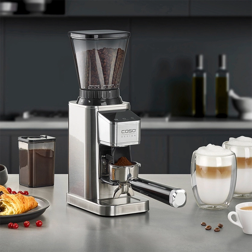 Moulin à café avec accessoires, café et pâtisserie sur une table.