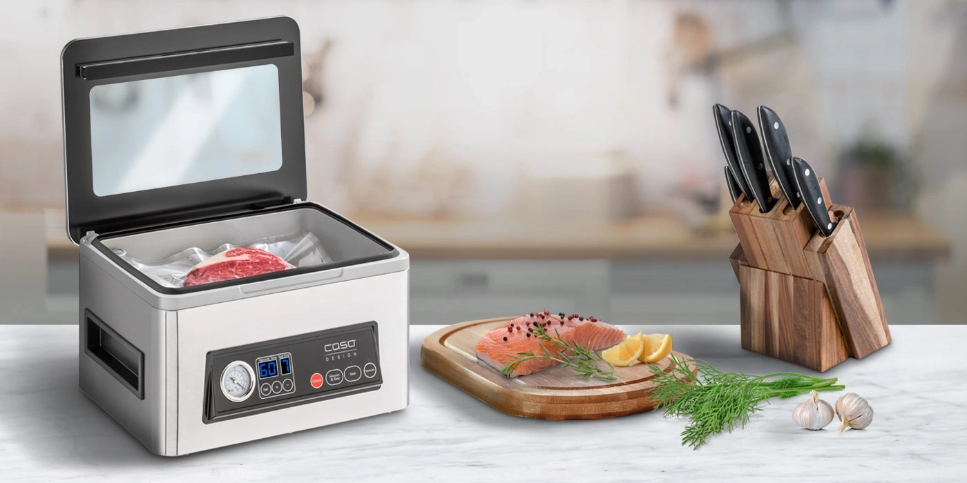 Ein Vakuumiergerät mit Fleisch, Lachs, Zitronen, Kräutern, Knoblauch und Messern.
