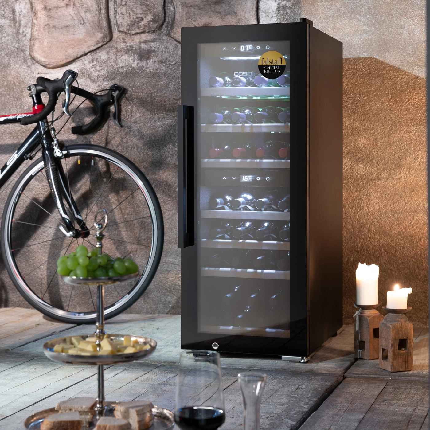 Weinkühlschrank, Fahrrad, Kerzen, Obst, Käse und Brot auf einem Holztisch.