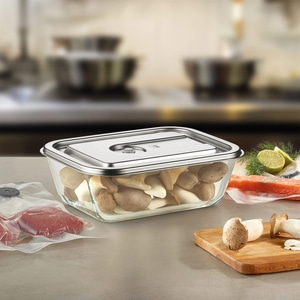 Glass container with mushrooms, meat, fish, and lemon on a kitchen countertop setting.