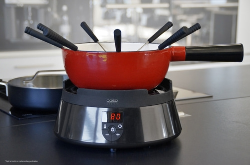 Roter Fondue-Topf mit schwarzem Griff und Gabeln auf einem schwarzen Heizgerät mit Temperaturanzeige.