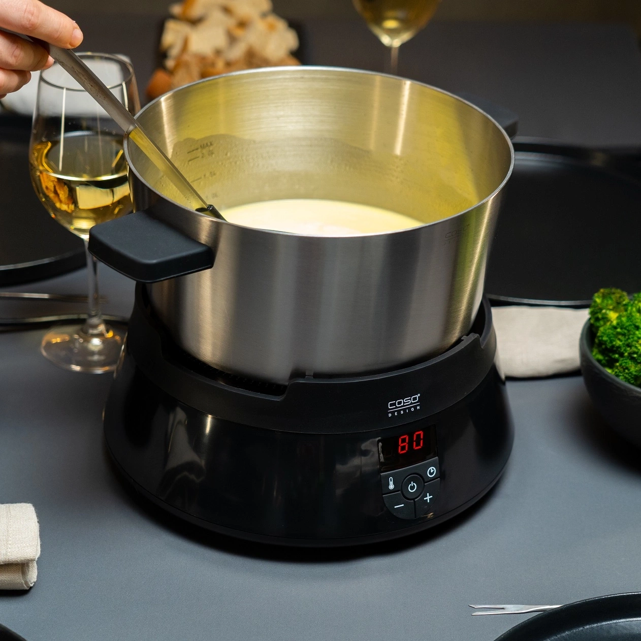 Ein Fonduetopf mit Käsefondue und Brotkorb im Hintergrund.