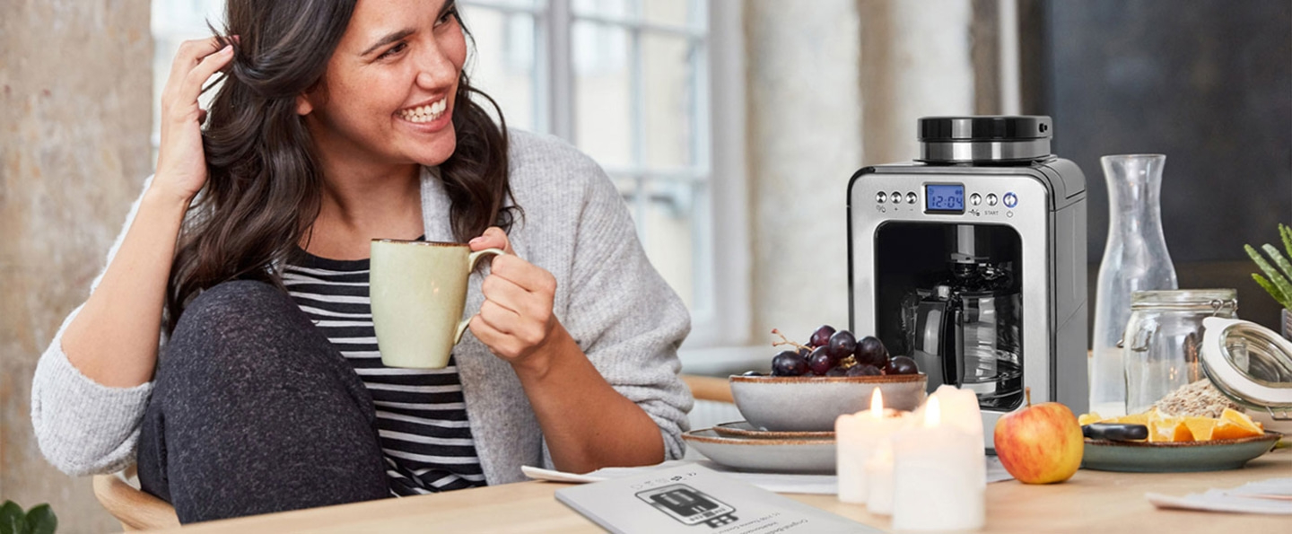 Femme buvant du café, cafetière, fruits, bougies, scène matinale détendue.