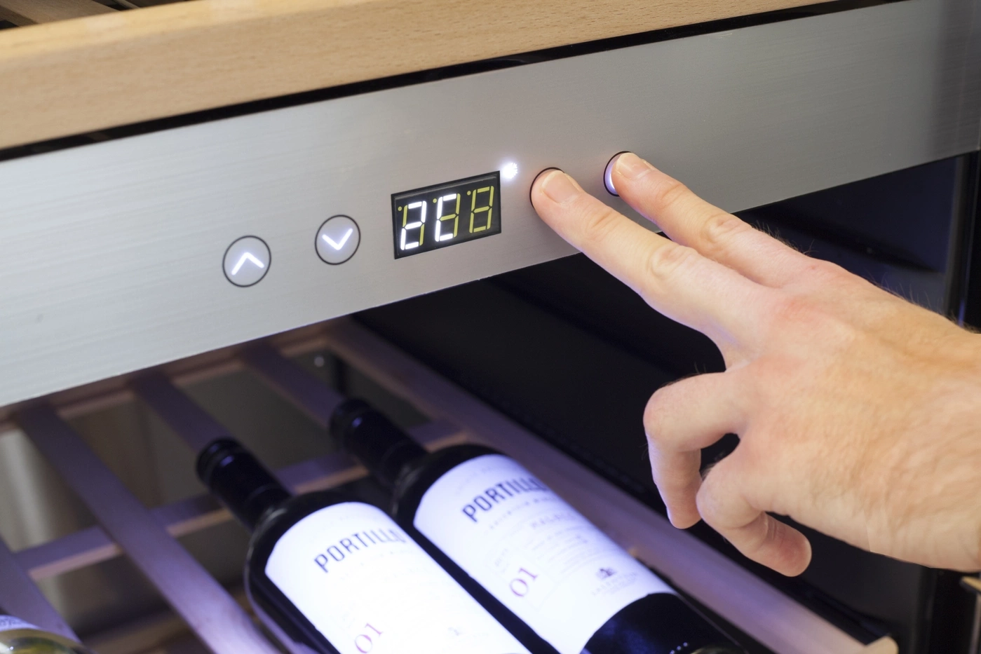 Hand drückt Knöpfe an einem Weinkühler mit digitaler Anzeige, die eine Temperatur anzeigt.