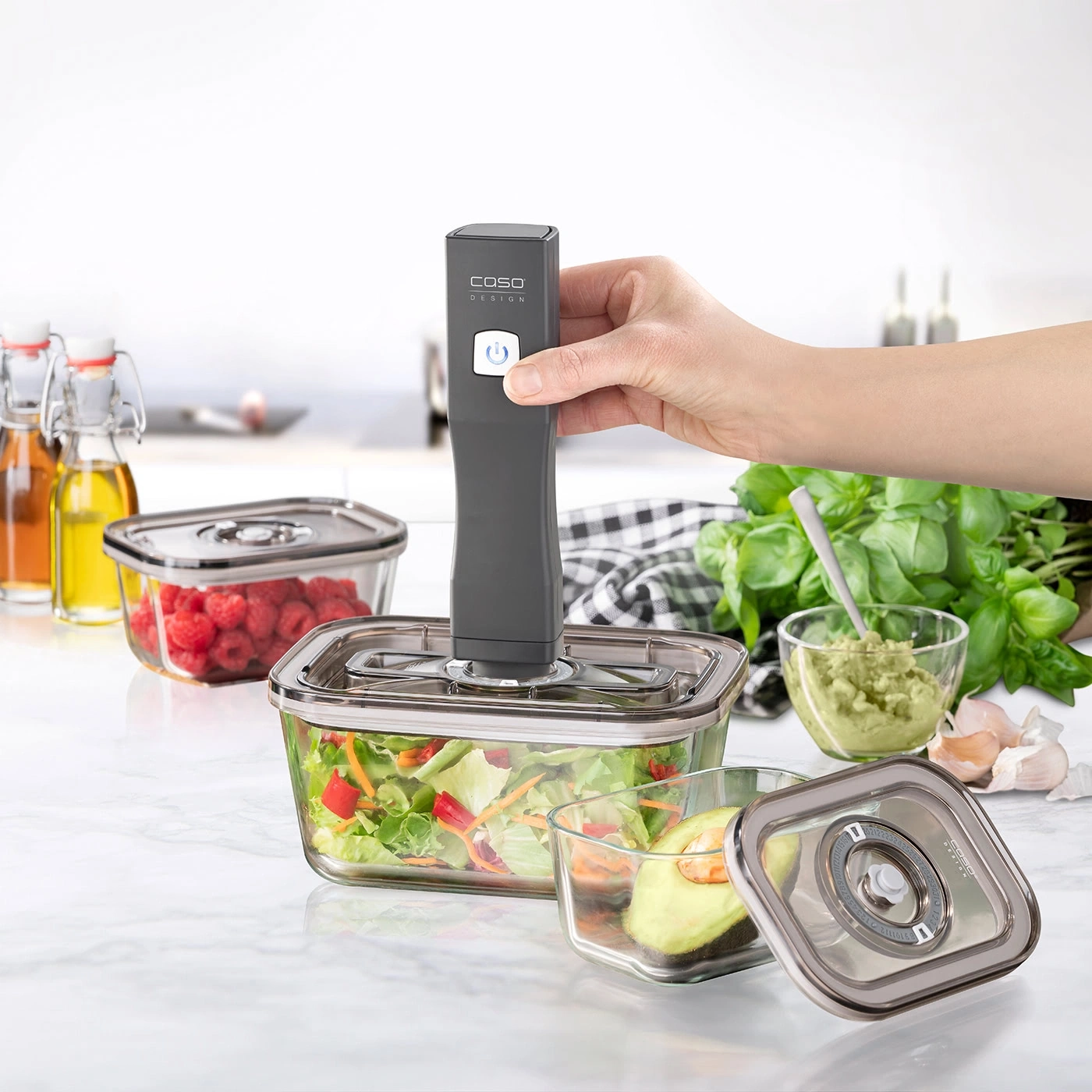 Eine Hand hält einen Vakuumierer über einem Salatbehälter.
