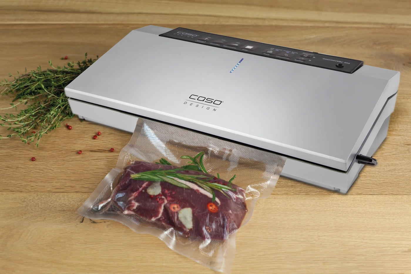 Vacuum sealer with meat and herbs on wooden surface. Caso Design GourmetVAC 380.