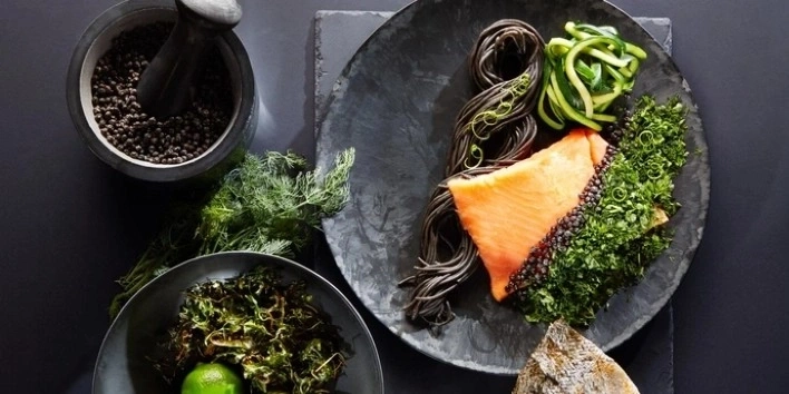 Lachs mit schwarzen Nudeln, Zucchini und Kräutern auf einem Teller.