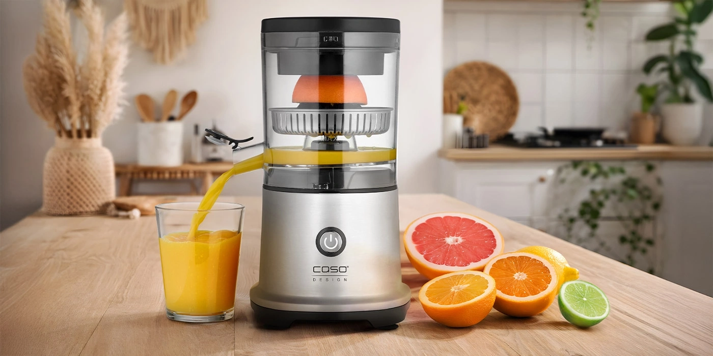 An electric citrus juicer with fresh fruits on a wooden table.