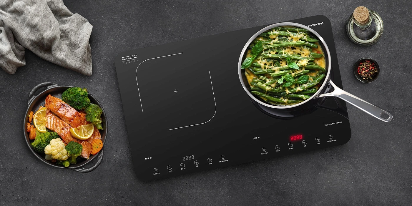 Une plaque à induction avec deux zones de cuisson et une casserole de haricots verts et de fromage.