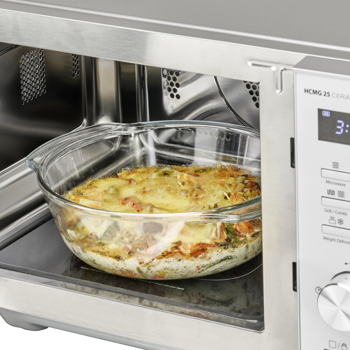 Microwave with casserole inside. Food being heated. Glass container. Stainless steel. Interior.