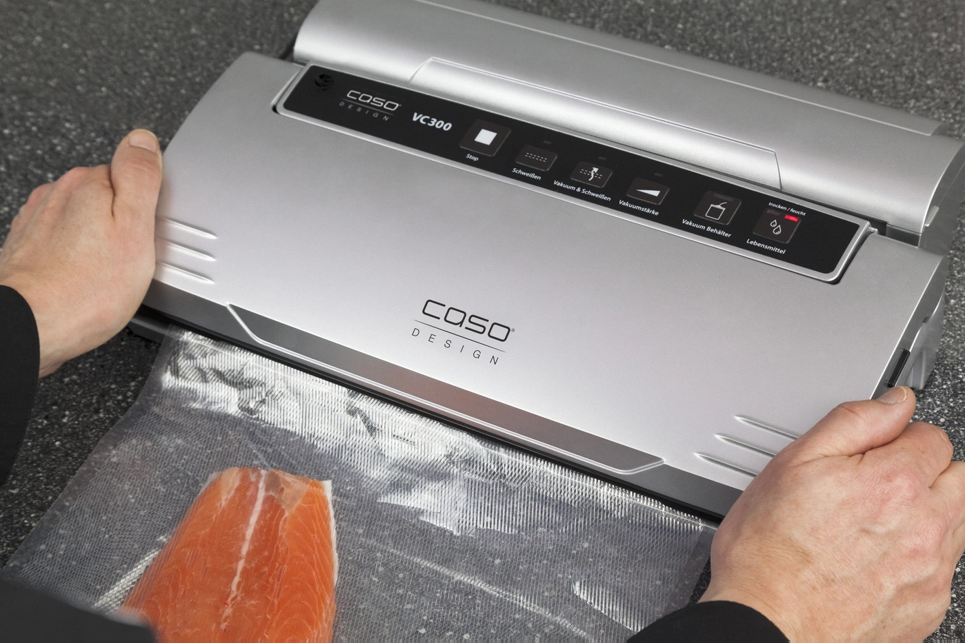 Person using a vacuum sealer with salmon. The device has the inscription COSO DESIGN VC300.