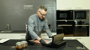 Mann in der Küche, der Lebensmittel vakuumverpackt, mit Caso-Logo und Geräten.