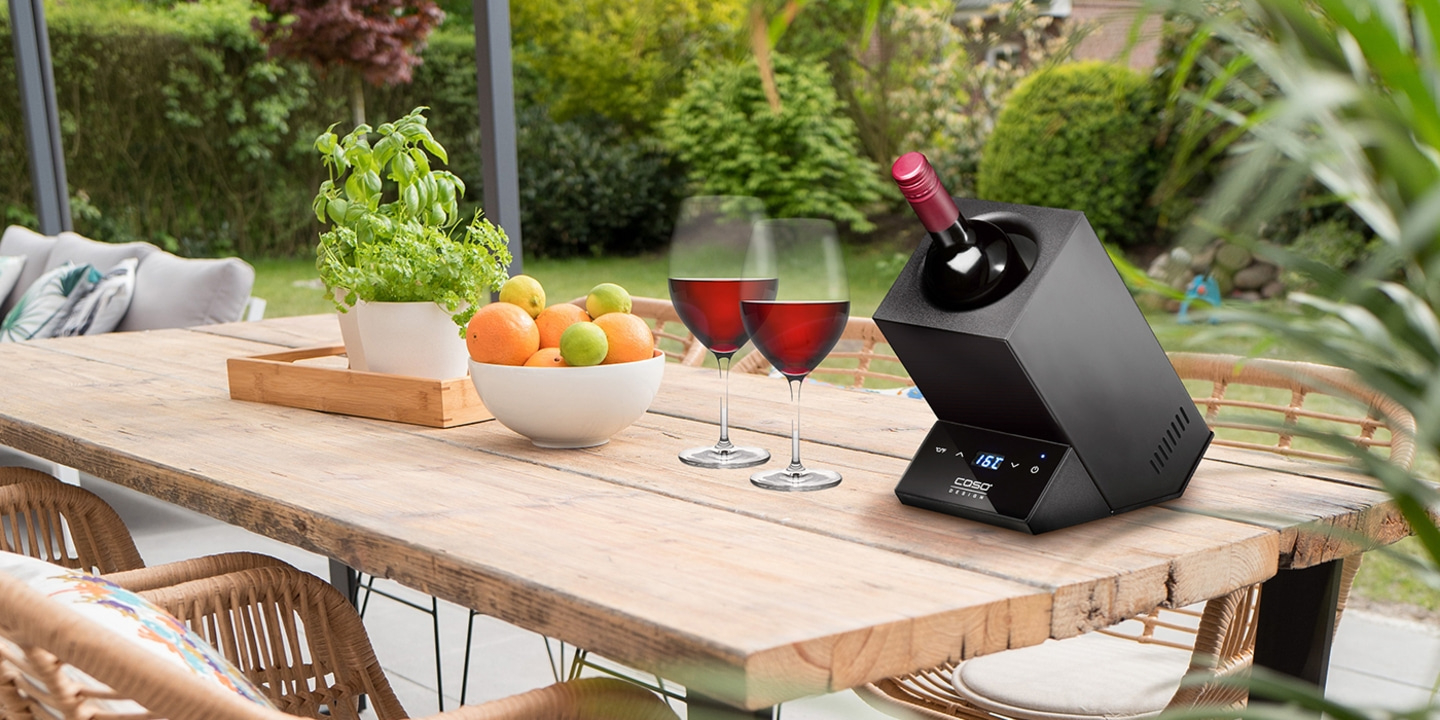 Holztisch mit Wein, Obst und Weinkühler im Garten bei Sonnenschein