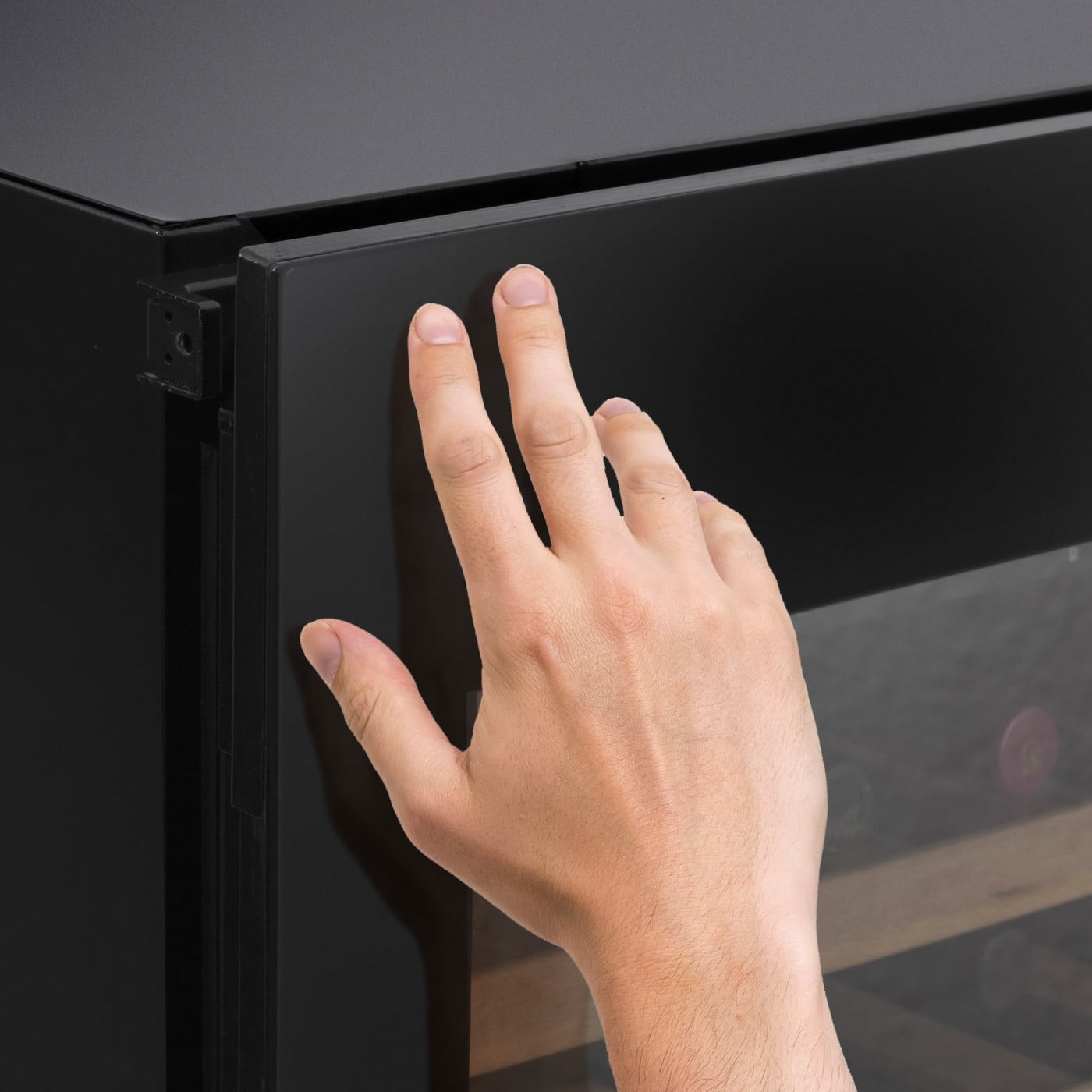 Hand touching black door of a refrigerator, close-up, fingers touching the surface