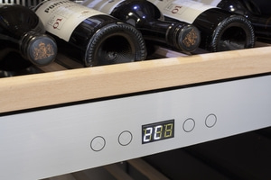 Wine cooler with temperature display and wine bottles nearby.