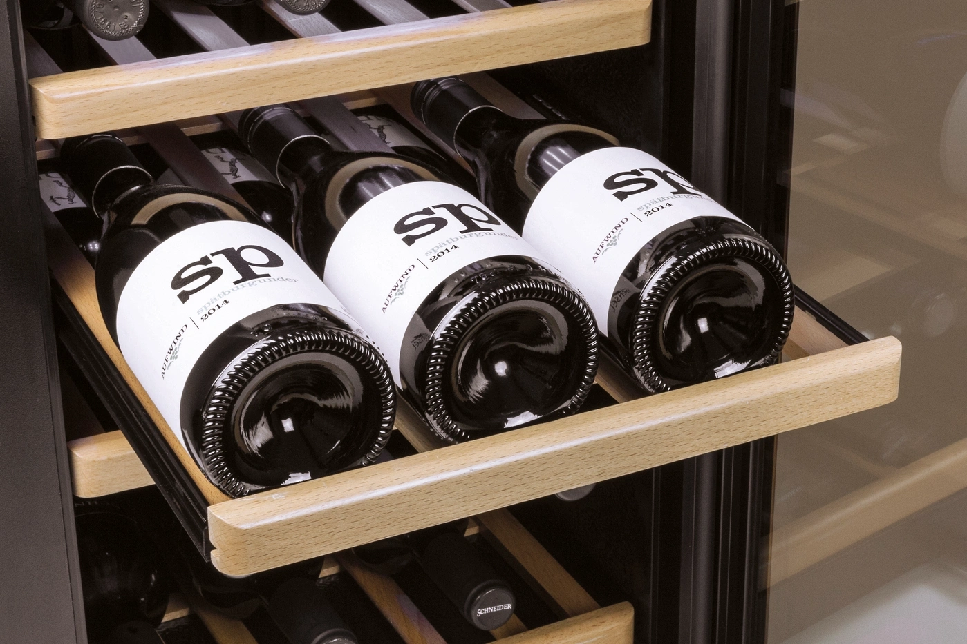 Weinflaschen in einem Weinkühlschrank. Aufwind Spätburgunder 2014. Holzregale und schwarzer Hintergrund.