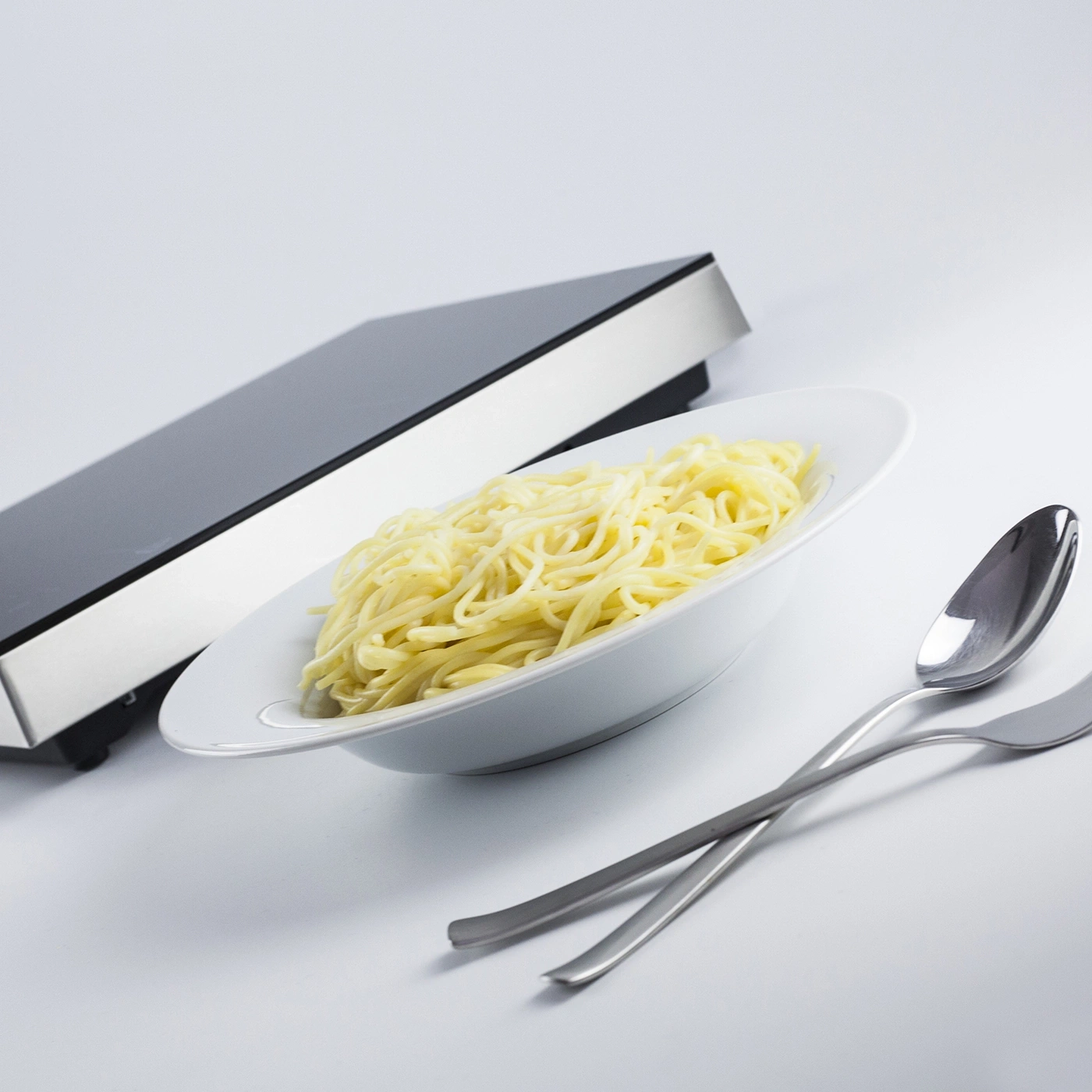 Ein Teller Spaghetti neben einem Induktionskochfeld mit Besteck.
