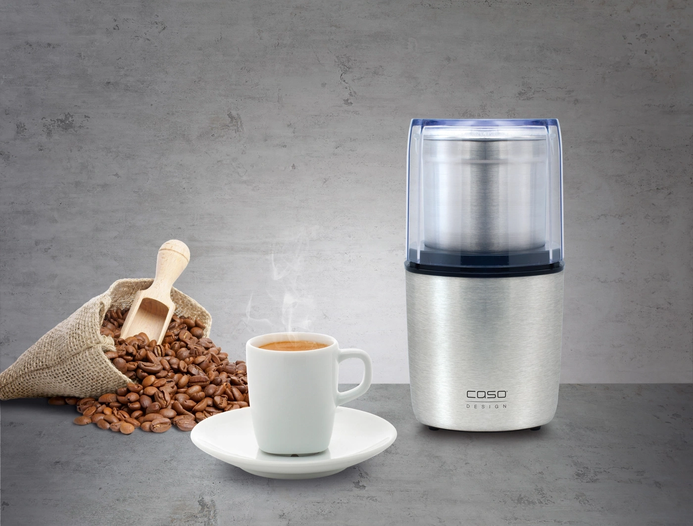 Kaffeemühle, Kaffeebohnen, Tasse Kaffee, Untertasse, Holzlöffel, Leinensack, Dampf, Design