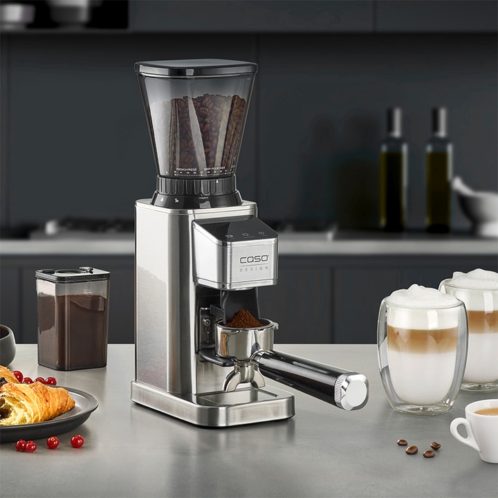Coffee grinder with accessories, coffee and pastry on a table.