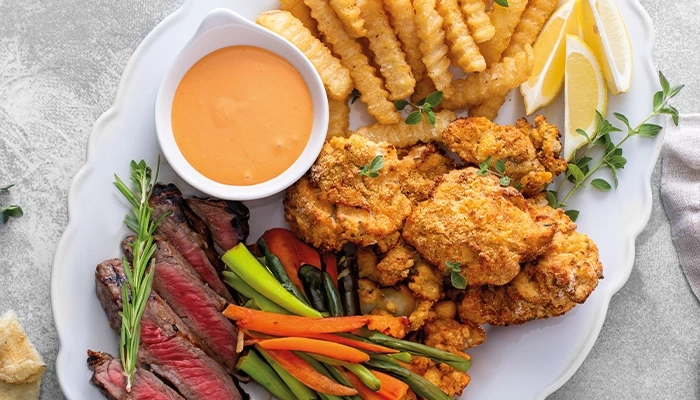 Ein Teller mit Steak, frittiertem Hähnchen, Pommes Frites und Gemüse.