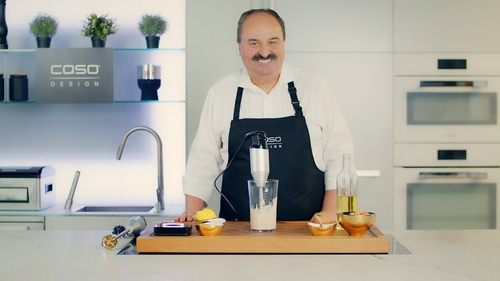 Man in kitchen with blender, ingredients for mayonnaise, Caso Design apron.