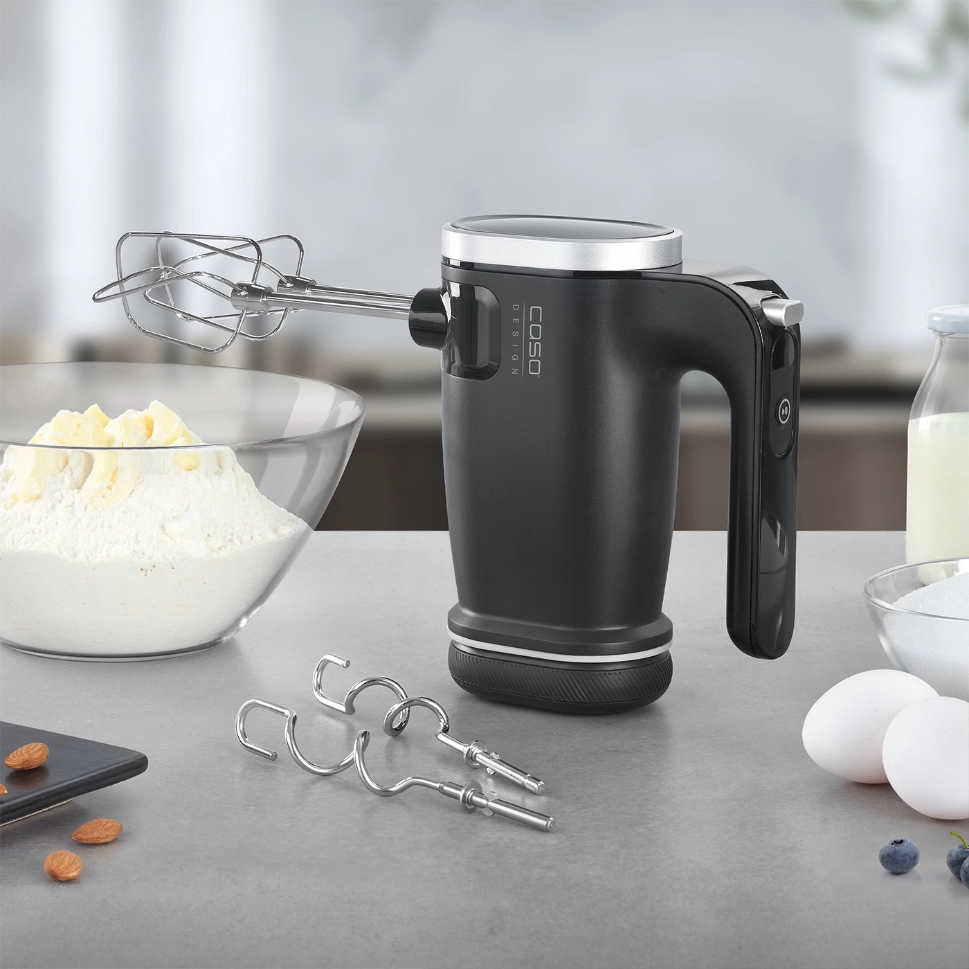 Mixeur à main noir avec accessoires sur une surface grise avec ingrédients.