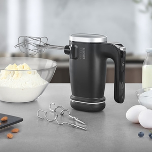 Schwarzer Handmixer mit Zubehör auf einer grauen Oberfläche mit Zutaten.