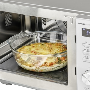 Microwave with casserole inside. Food being heated. Glass container. Stainless steel. Interior.