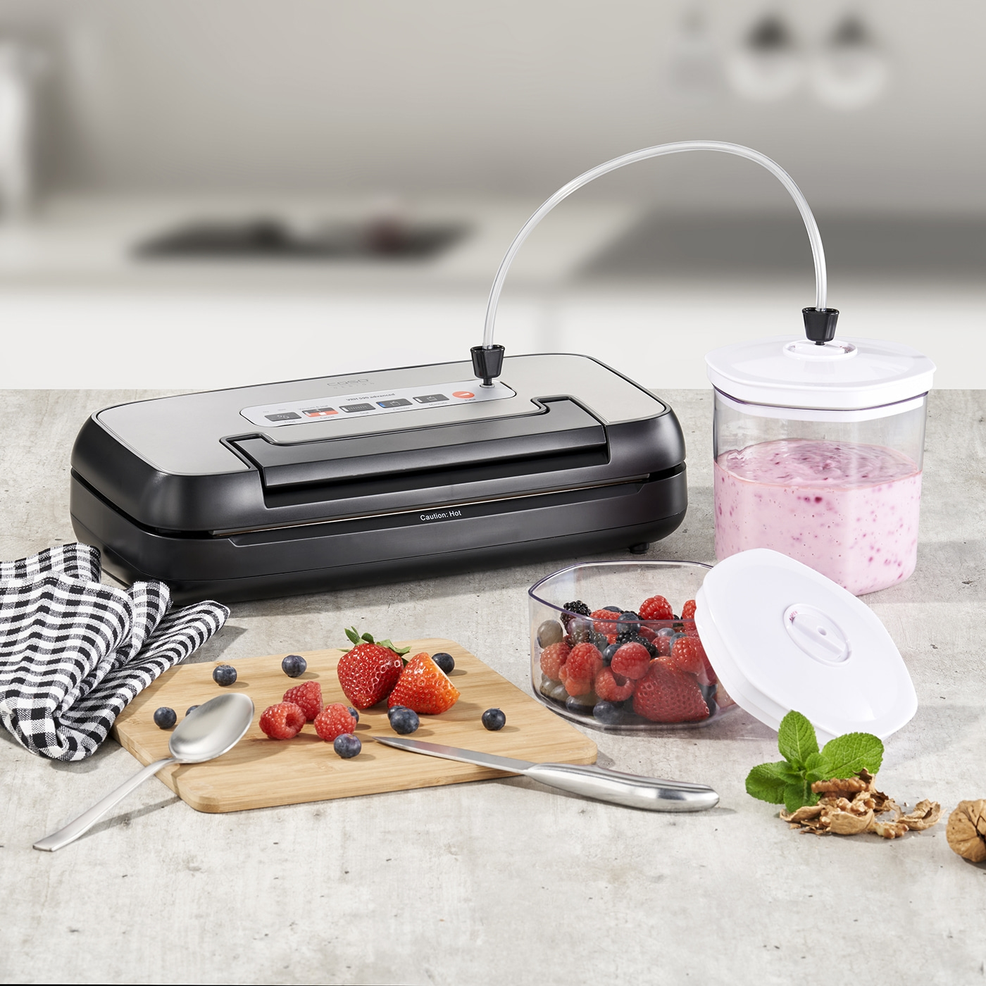 Vakuumiergerät mit Beeren, Smoothie und Zubehör auf einer Arbeitsplatte.