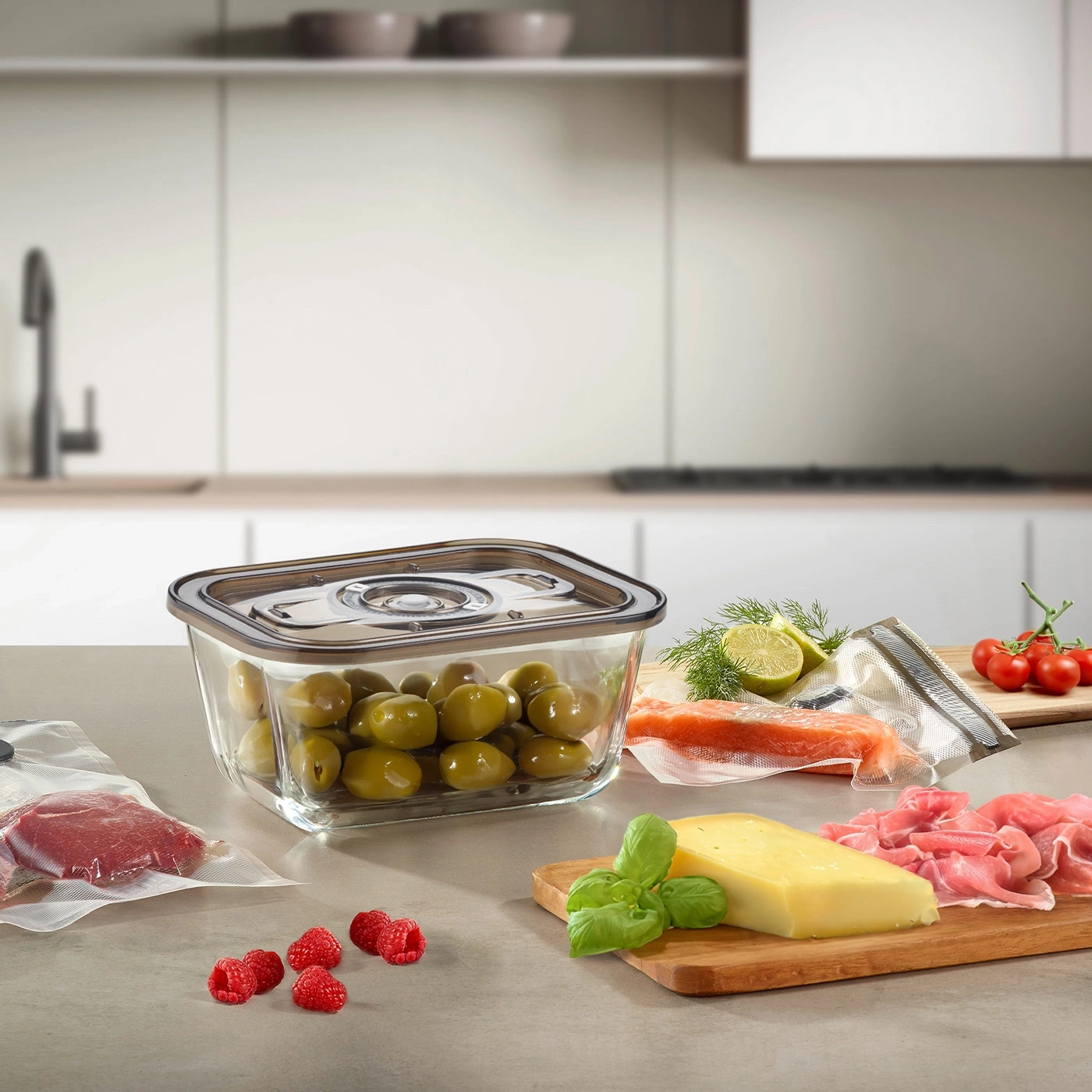 Food on a kitchen counter: olives, raspberries, cheese, salmon, tomatoes, and prosciutto.