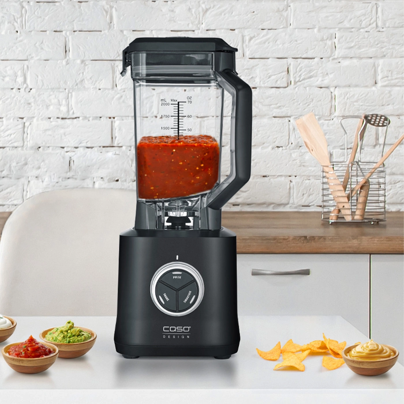 Black blender with salsa, tortilla chips, and dips on a kitchen table setting.