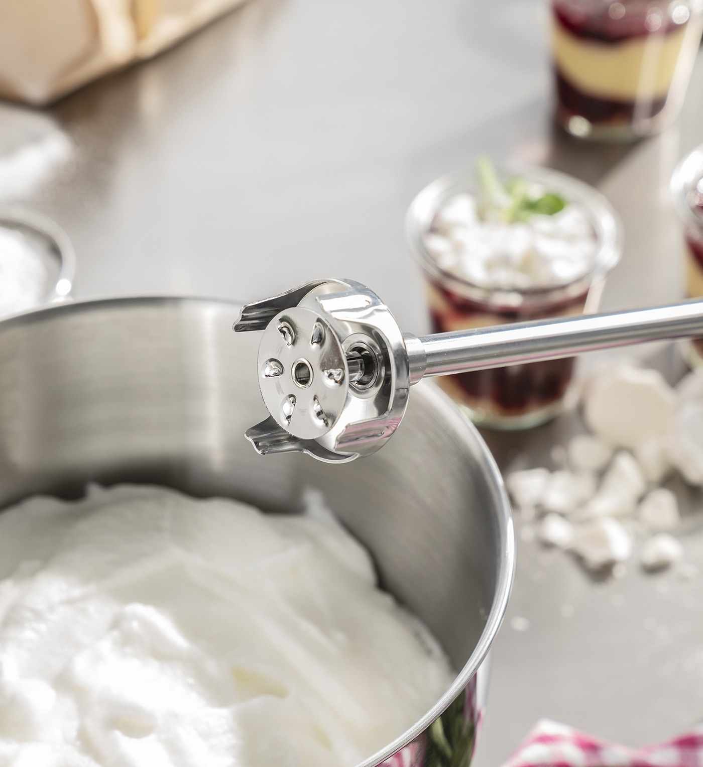 Edelstahl-Mixer in einer Schüssel mit geschlagenem Eiweiß und Dessertgläsern.