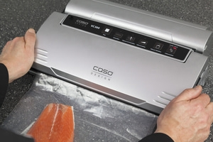 Personne utilisant une machine à sceller sous vide avec du saumon. L'appareil porte l'inscription COSO DESIGN VC300.