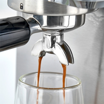 Nahaufnahme einer Espressomaschine, die Kaffee in ein Glas brüht.