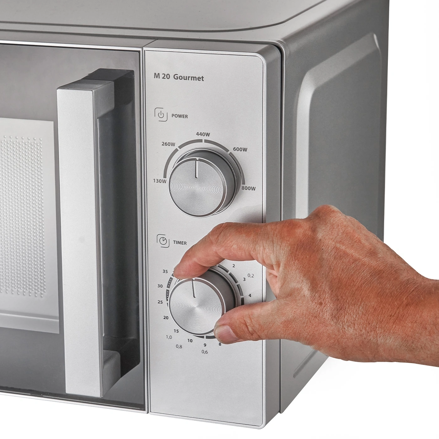 Eine Hand dreht den Timer-Regler an einer Mikrowelle.