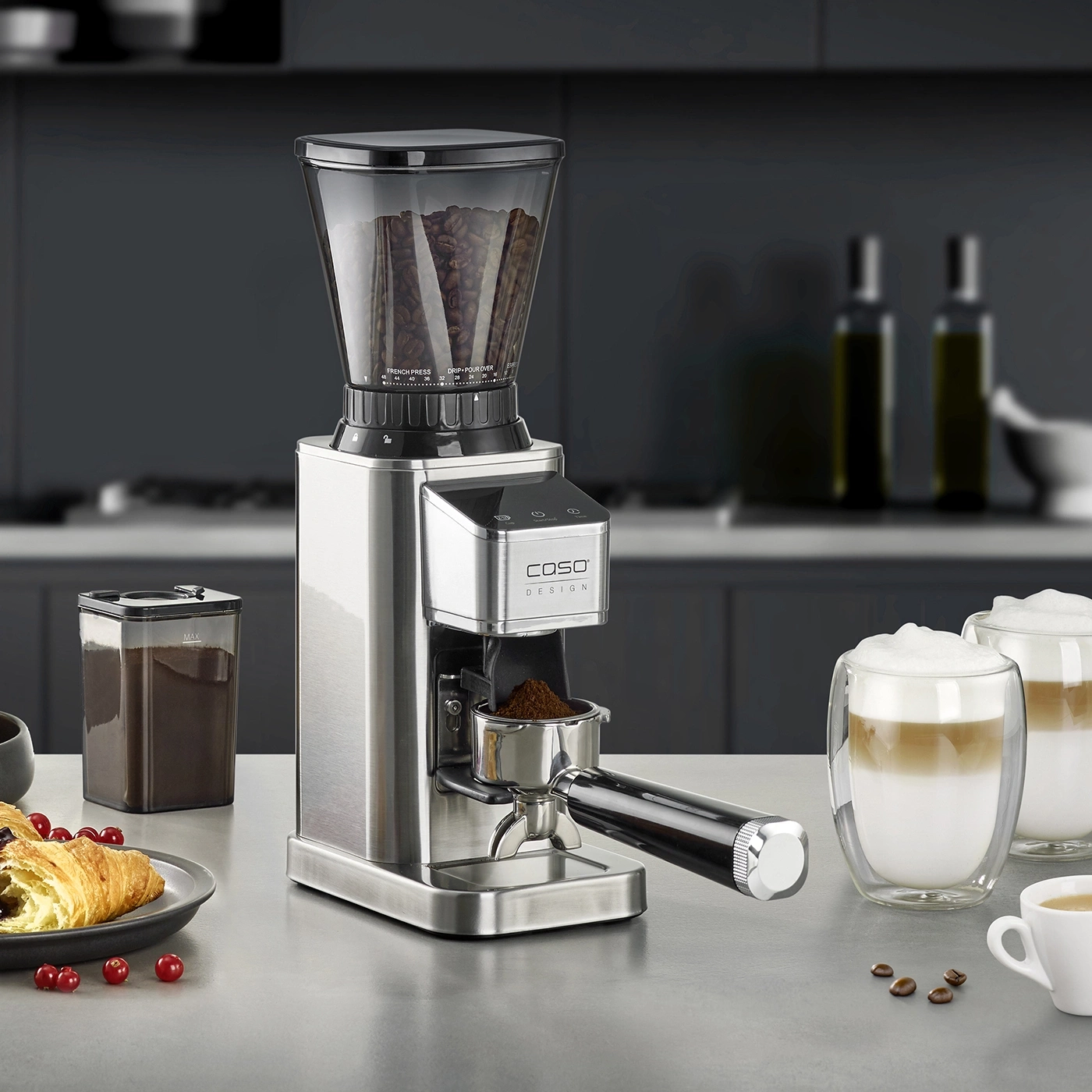 Moulin à café avec accessoires, café, croissant, boissons sur un comptoir.