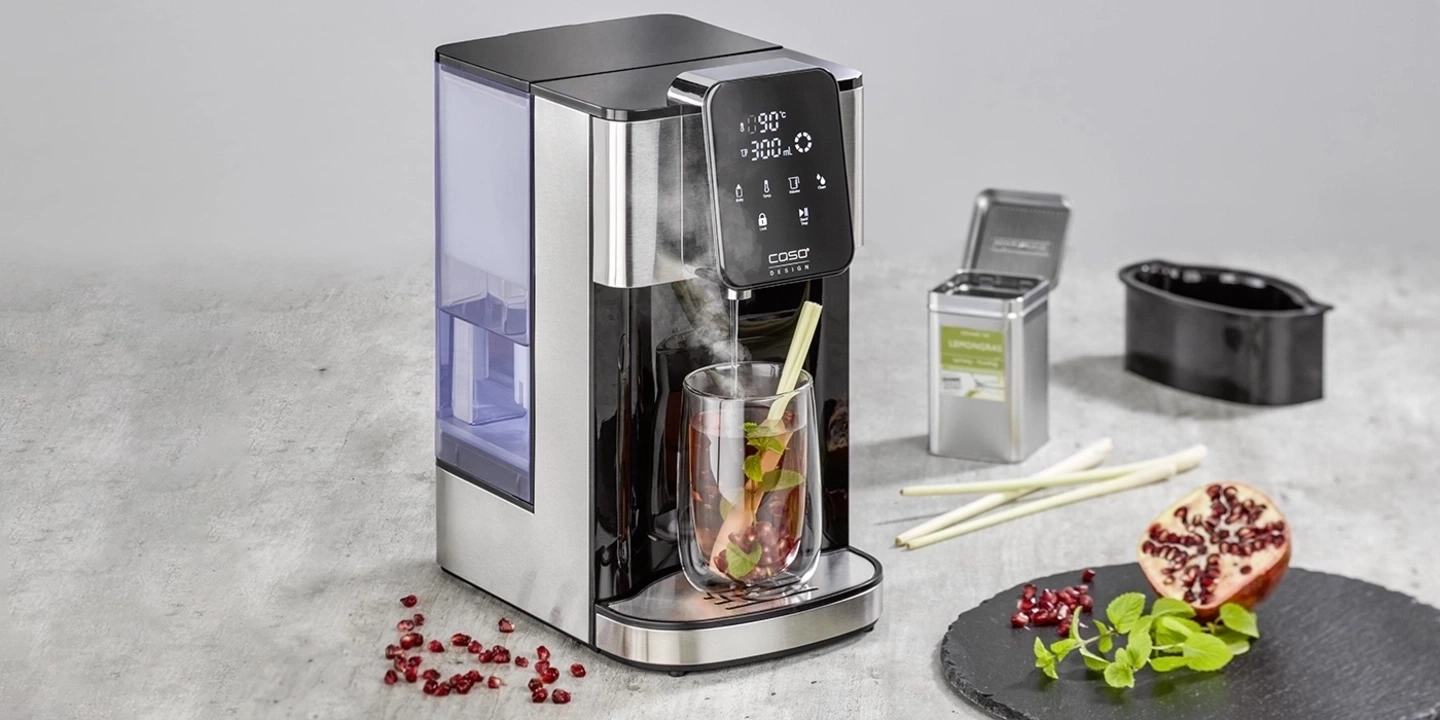 Teemaschine mit Glas, Zitrone, Granatapfel und Kräutern auf einem Tisch