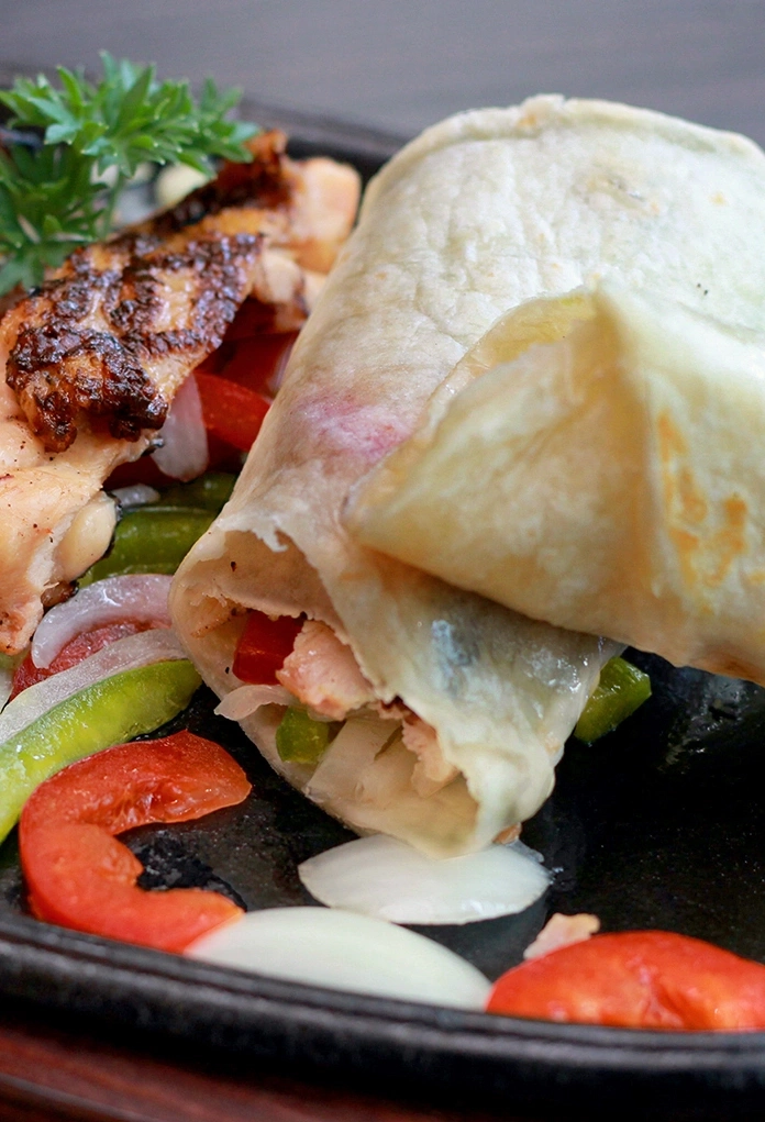 Ein Hähnchen-Wrap mit gebratenem Hähnchen, Paprika und Zwiebeln auf einem heißen Teller.