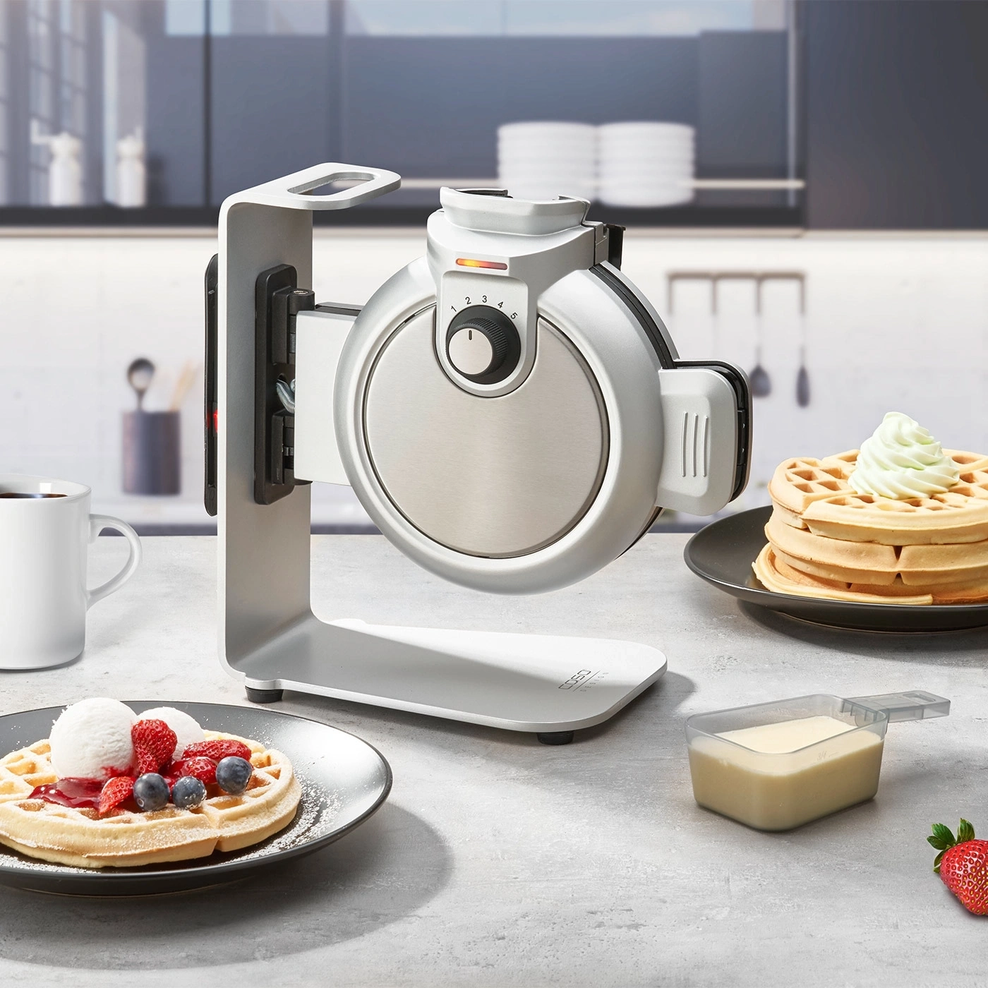 Waffeleisen mit Waffeln und Beeren auf einem Tisch in der Küche.