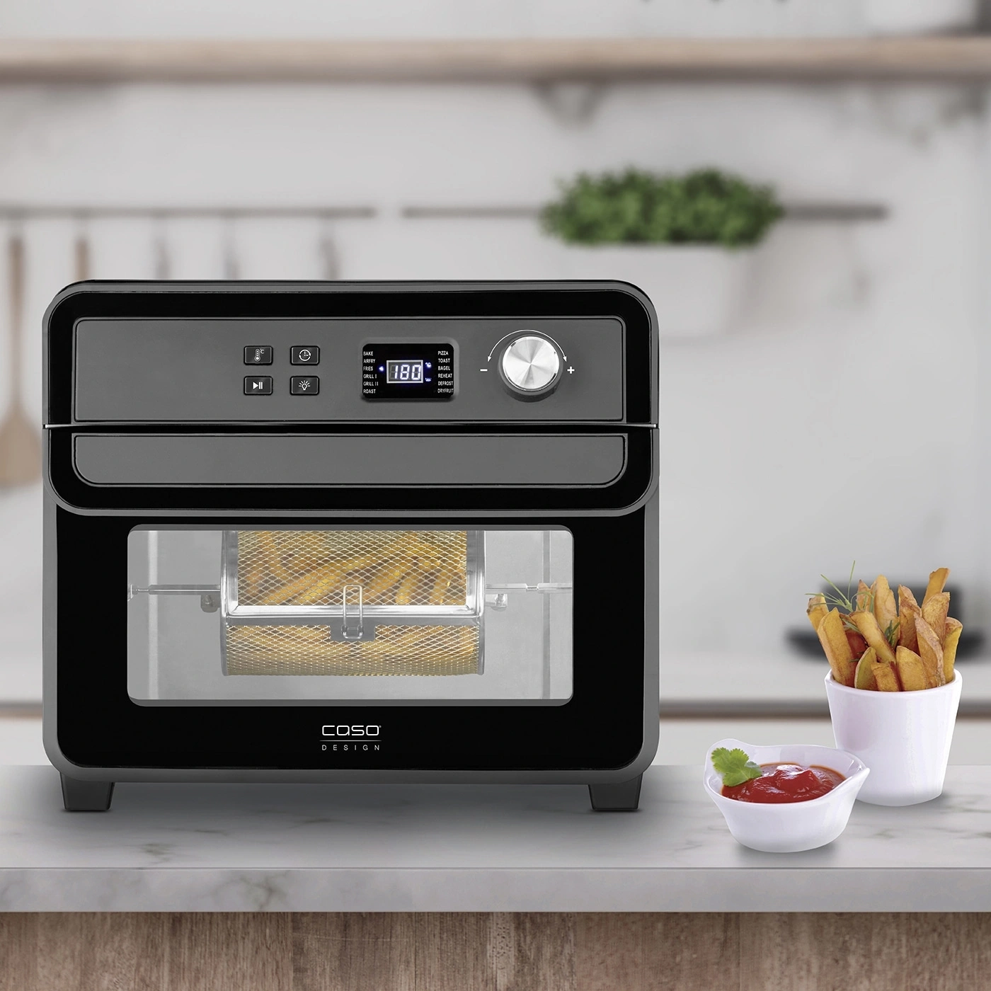 Black air fryer with fries, ketchup, and herbs on a marble surface, ready to eat.