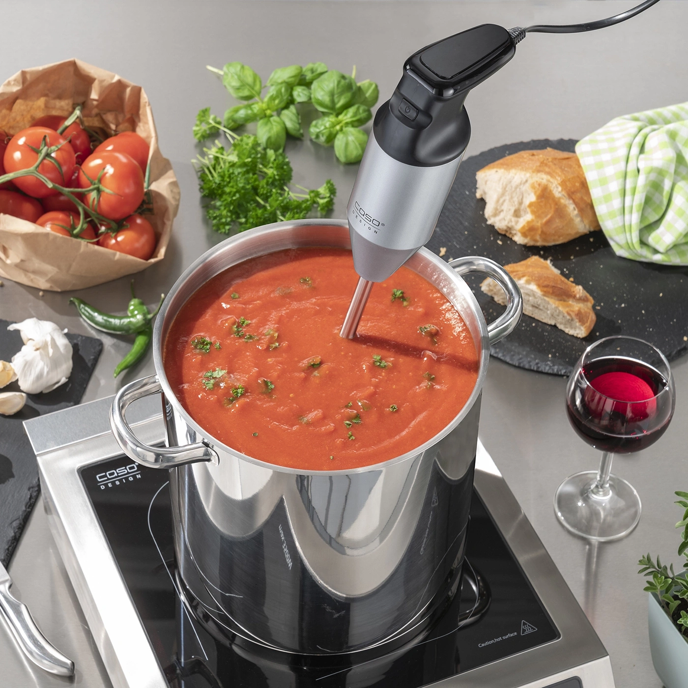 Tomatensuppe wird mit einem Stabmixer zubereitet, mit Zutaten wie Brot und Wein.