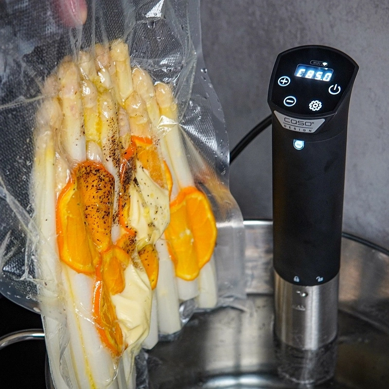 Spargel mit Orangen und Butter im Vakuumbeutel, Sous-vide-Gerät daneben.