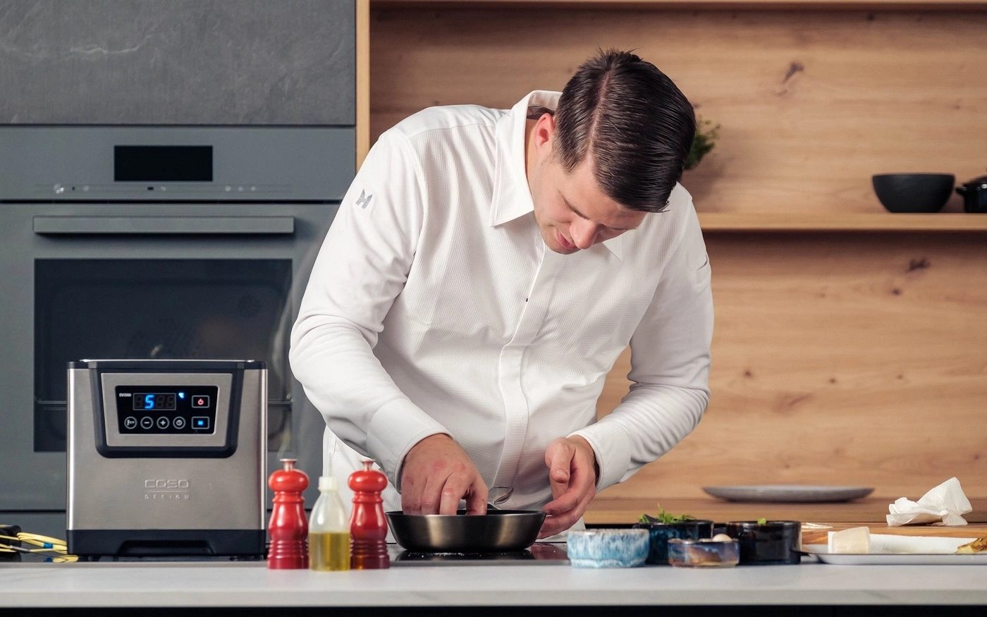 Koch in weißem Hemd bereitet Essen in einer Küche zu.
