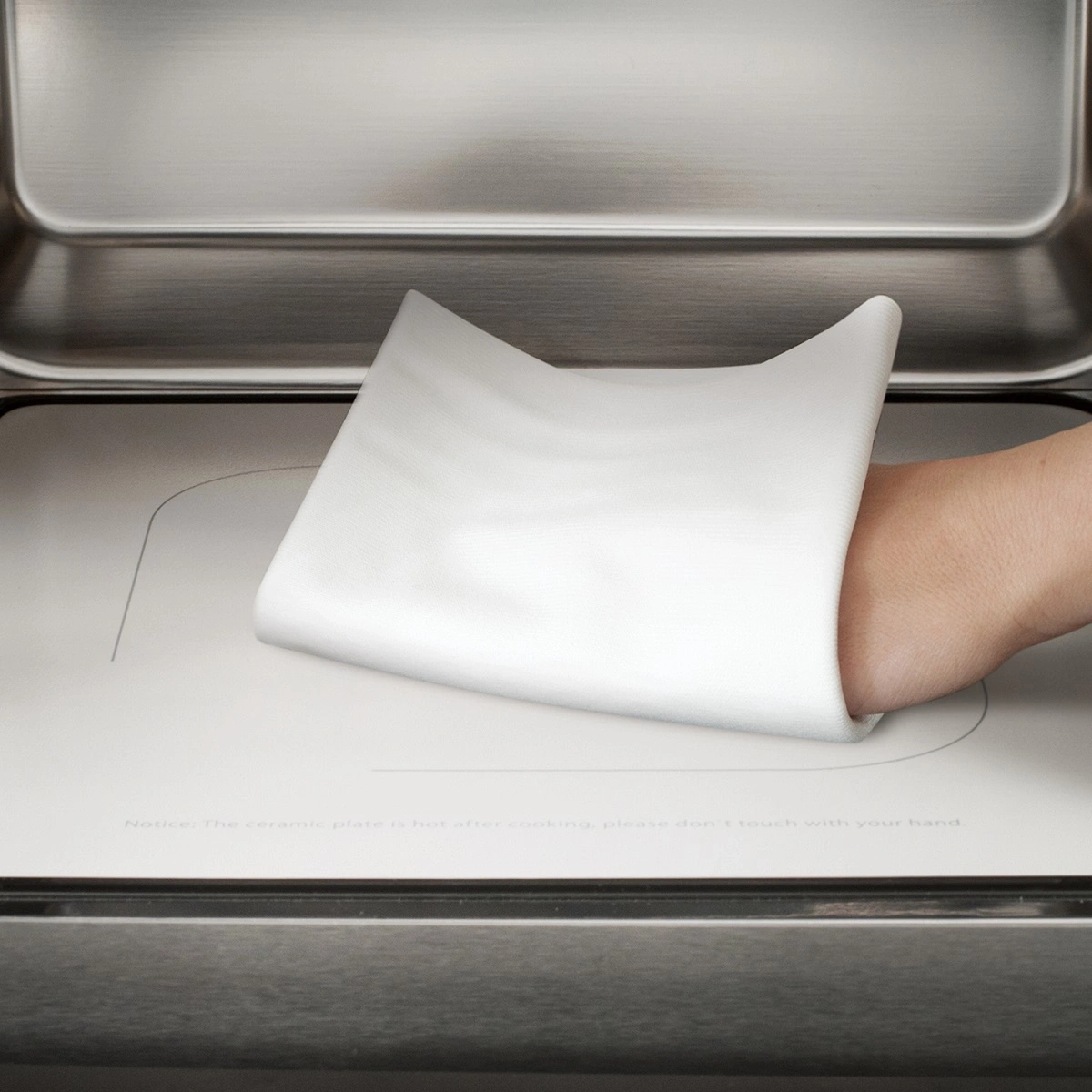 Hand mit Tuch auf heißer Keramikplatte