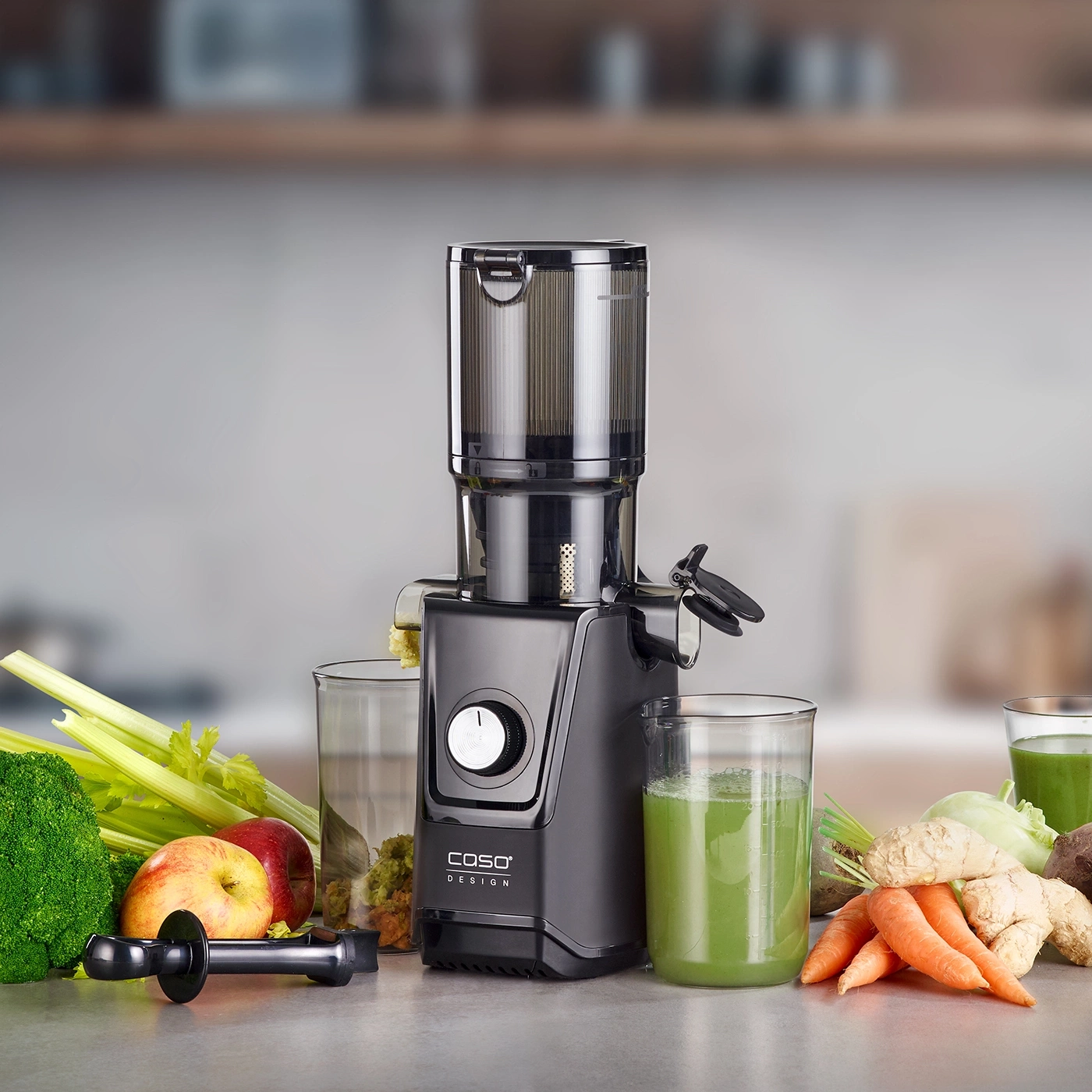 Extracteur de jus noir avec légumes et verres de jus sur un comptoir
