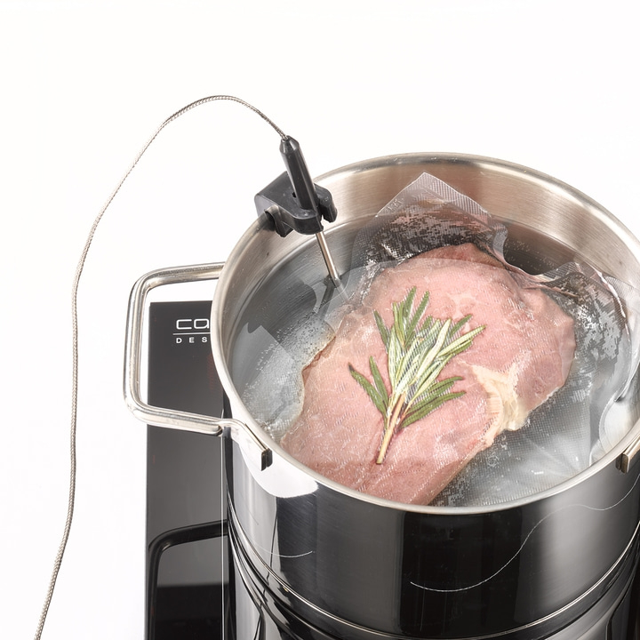 Meat being sous vide in a pot with rosemary, cooking process.