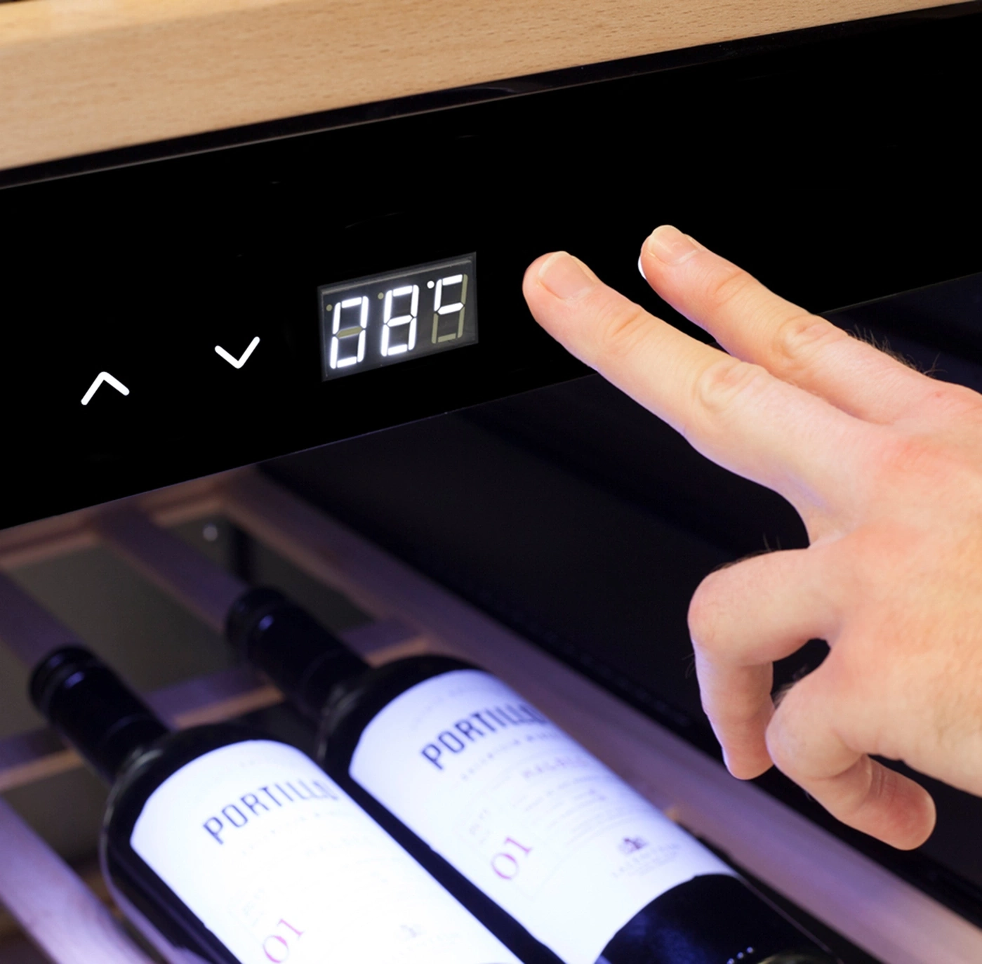 Weinkühler mit Temperaturanzeige und Bedienung durch Finger, Weinflaschen im Hintergrund