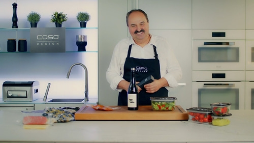 Mann in der Küche mit Essen und Wein, Caso Design Logo im Hintergrund.